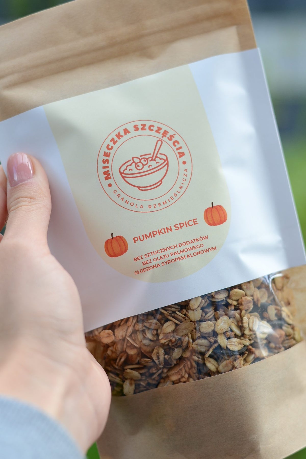 Torebka granoli Pumpkin Spice trzymana w dłoni, widoczna etykieta z dyniami